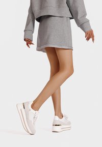 Sneaker platform bianchi con accenti testurizzati e un dettaglio metallico oro. Abbinati a una felpa oversize grigia e a una gonna.