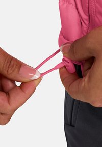 Nahaufnahme einer Hand, die einen pinken Kordelzug an einer leichten Jacke justiert. Die Textur ist glatt, mit einem eleganten Design und kontrastierendem schwarzem Material darunter.