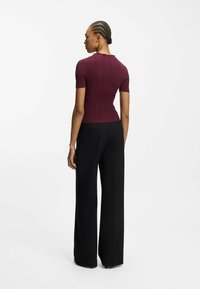 Bordowa prążkowana bluzka z krótkim rękawem i falbankowym dekoltem, zestawiona z czarnymi szerokimi spodniami z wysokim stanem, widziana od tyłu.