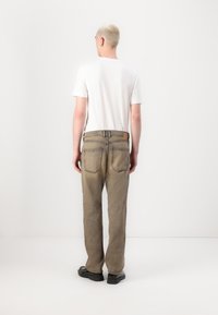 Beige jeans with a straight leg fit, textured fabric, five pockets, and visible stitching details. Worn with a plain white t-shirt.