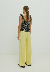 Top negro con estampado floral y tirantes con volantes, combinado con pantalones amarillos de pierna ancha. La tela parece ligera y texturizada.
