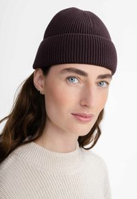 Dark purple knit beanie with ribbed texture and a tapered top, worn by a person with long hair, complementing a light-colored sweater.