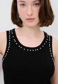 Zwarte tanktop met zilveren studs langs de halslijn en schouders, gemaakt van een rekbaar materiaal, aansluitende pasvorm en eenvoudig ontwerp.