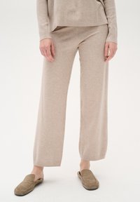 Pantaloni lounge beige a gamba larga realizzati in morbido tessuto a maglia, abbinati a scarpe slip-on marroni chiari. Design semplice con dettagli a costine in vita.