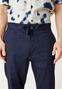 Mörkblå linbyxor med dragsko i midjan. Slät textur, ledig passform, med en framficka och diskreta sömdetaljer.