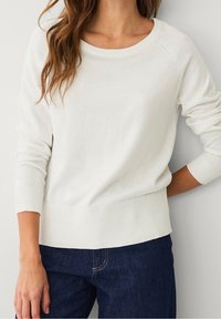 Pull en maille blanc avec encolure ronde, poignets et ourlet côtelés. Manches longues et coupe décontractée, associé à un jean en denim foncé.