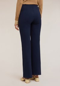Marineblauwe wijde broek met een gladde textuur, voorzien van een hoge taille en minimale naaddetails, gecombineerd met lichtgekleurde blokhak schoenen.