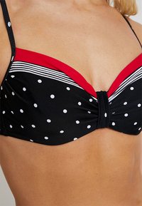 Zwarte bikinitop met polka dots, versierd met rood-witte gestreepte accenten, met een gedraaide middenstuk en verstelbare bandjes.