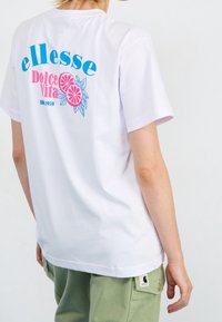 Witte katoenen t-shirt met kleurrijke tekst op de voorkant en een citrusgrafiek. Korte mouwen met een ontspannen pasvorm, gecombineerd met groene broek.