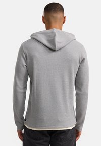 Grijze hoodie met een textuurafwerking, lange mouwen en een aansluitend ontwerp. Heeft een achterhoood en een contrasterende witte binnenlaag bij de zoom.