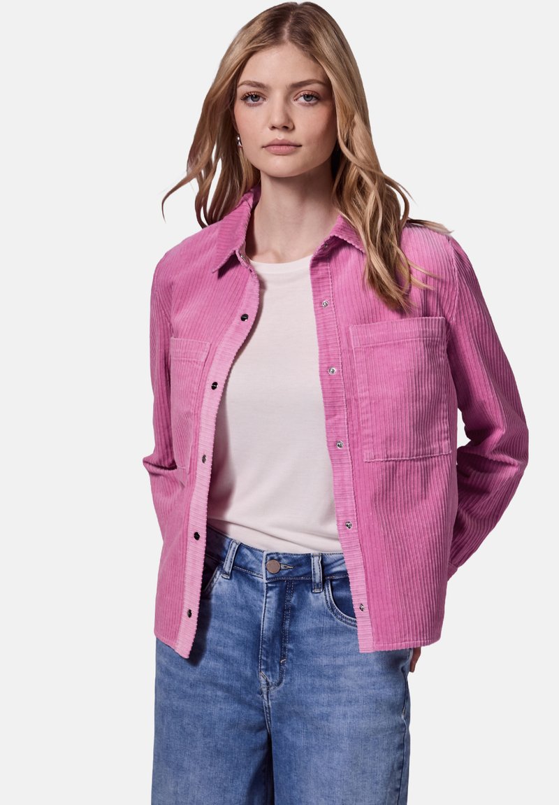 Rosa kordfløyelskjorta med knapplukking, lange ermer og to brystlommer, iført over en hvit t-skjorte og parret med blå jeans.