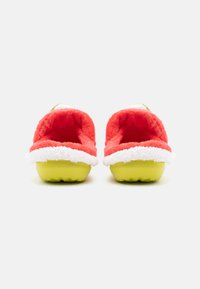 Red fluffy slippers with white trim and green accent, rounded back, rubber sole, and textured grip. Designed for comfort and warmth.