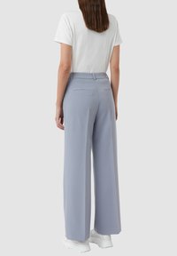 Jasnoniebieskie spodnie o szerokich nogawkach o gładkiej fakturze, z dwiema tylnymi kieszeniami i średnim stanem, zestawione z białą koszulką.