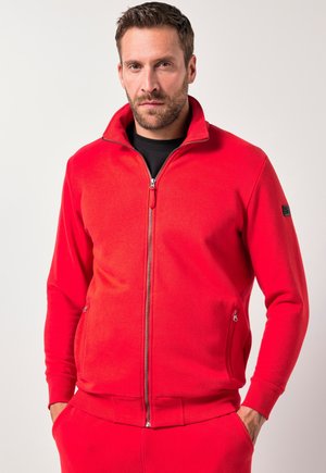 Rote Fleecejacke mit Reißverschluss und hohem Kragen, seitlichen Taschen und einer glatten Textur. Kombiniert mit roten Jogginghosen im passenden Farbton.