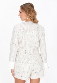 Conjunto de tweed blanco que incluye un top estructurado y pantalones cortos con un patrón de cuadrícula. Presenta puños blancos y sencillos acentos de botones.