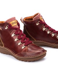 Bottes chelsea en cuir marron avec des lacets bordeaux et ferrures dorées. Elles disposent d'un col en tricot texturé et d'une semelle rembourrée pour le confort.
