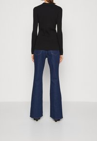 Haut noir à manches longues associé à un jean bleu évasé à taille haute, avec une texture lisse et des détails de coutures visibles.