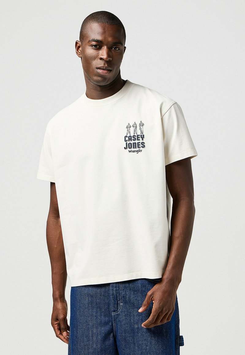 Camiseta corta de manga con estampado gráfico de tres figuras y el texto "CASEY JONES" en azul, hecha de suave tela de algodón.