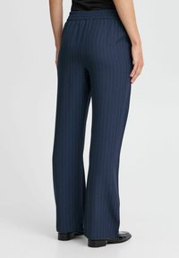 Pantalons bleu marine à rayures avec une coupe décontractée, dotés d'une taille élastique et de jambes évasées, associés à des chaussures noires.