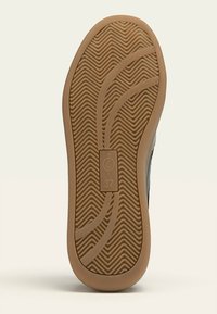 Semelle de basket noire avec un dessous en caoutchouc brun texturé. Présente des motifs de bande de roulement en zigzag et un logo circulaire avec la taille 37.