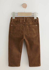 Pantalon pour tout-petit en velours côtelé marron avec taille élastique et deux poches arrière, suspendu à un cintre en bois sur un fond blanc.