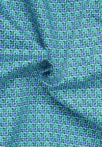 Katoenen stof met een turkooizen achtergrond en een herhalend patroon van groene en blauwe bladeren, geaccentueerd door zwarte stippen. Soepele textuur.
