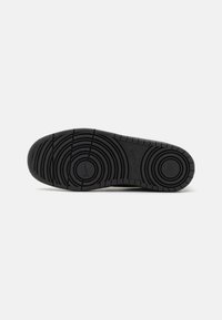 Schwarze Gummisohle eines Sneakers mit einem kreisförmigen Profil, glatten Kanten und geprägtem Branding an der Seite.