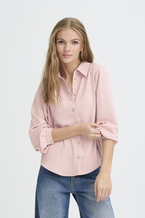 Helles rosa Hemd mit langen Ärmeln, gerafften Manschetten, glatter Textur und abgerundetem Saum, kombiniert mit blauen Jeans.