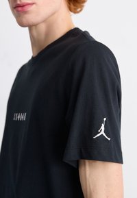 T-shirt nera in cotone con maniche corte, colletto a girocollo e logo Jumpman bianco ricamato sulla manica sinistra.