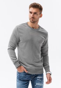Grijze sweatshirt van een zacht materiaal, met een ronde halslijn, geribbelde manchetten en onderrand, gecombineerd met versleten blauwe jeans. Casual pasvorm en ontwerp.