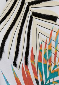 Close-up van stof met zwarte geborduurde lijnen en een kleurrijk abstract bladpatroon in oranje, teal en geel op een witte achtergrond.