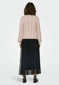 Un pull en maille torsadée rose clair avec de longues manches bouffantes, associé à une jupe noire plissée de longueur cheville et des chaussures noires à talons.