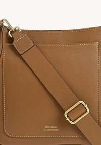 Sac bandoulière en cuir marron avec une finition texturée, dotée d'une poche avant, d'une sangle ajustable et d'accents en métal doré.