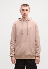 Lichtbruine hoodie van zacht materiaal, met een kanga-roe pocket, trekkoord capuchon en een klein logo detail op de borst.