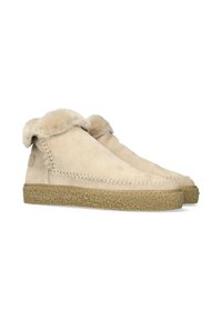 Botas de tobillo de piel de oveja con un suave y esponjoso collar, parte superior de ante beige y suela de corcho texturizada. Detalle de costura visible a lo largo de los bordes.