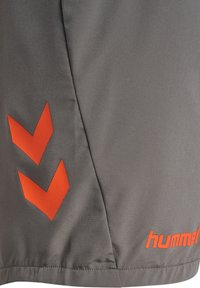 Gråa sportshorts med ett orange chevronmönster och logotyp. Tyget ser mjukt ut med en sydd fåll.