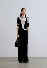 Čierny a biely vzorovaný pletený sveter s krátkymi rukávmi, kombinovaný so širokými čiernymi nohavicami a malou čiernou kabelkou s hladkou textúrou.