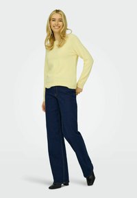 Pull en maille jaune pâle associé à un jean en denim bleu foncé à jambes larges. Pull au toucher doux, au design simple et avec des coutures jaunes contrastantes.