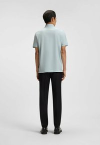 Ljusblå kortärmad polo med en slät textur, kombinerad med svarta raka byxor och svarta skor, sedd bakifrån.