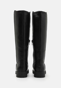 Bottes en cuir noir hautes jusqu'aux genoux avec une texture lisse, des zips à l'arrière et des semelles renforcées. Présente un surpiquage décoratif sur les côtés.