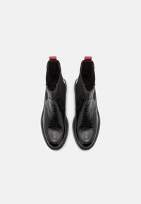 Bottines en cuir noir avec texture crocodile, panneaux latéraux élastiques, bouts ronds et languettes rouges à l'arrière, vues de dessus.