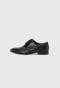Zapato de vestir de cuero negro con punta afilada, diseño de cordones, textura suave y acentos minimalistas, que cuenta con un tacón bajo y apilado.