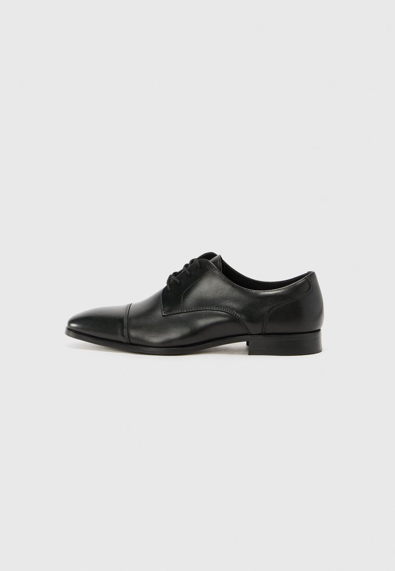 Zapato de vestir de cuero negro con punta afilada, diseño de cordones, textura suave y acentos minimalistas, que cuenta con un tacón bajo y apilado.