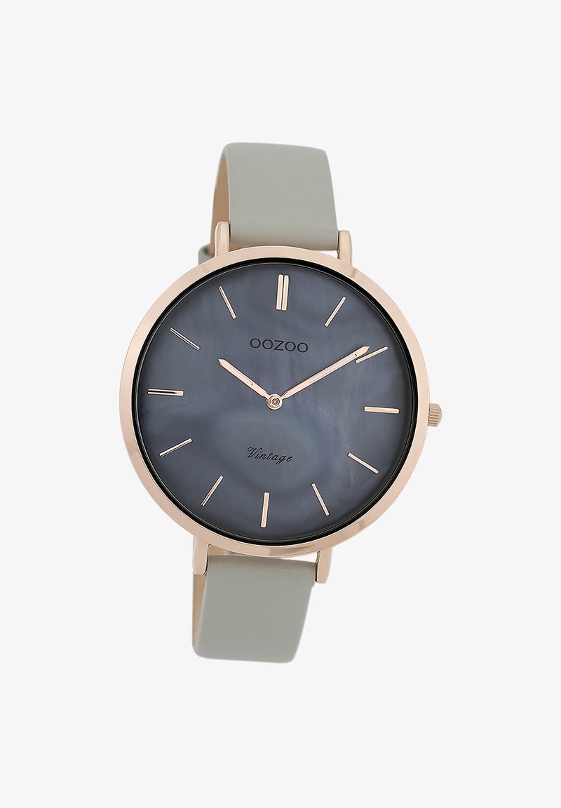 Montre en or rose avec un cadran en mère perlée gris foncé, des index horaires minimalistes et un bracelet en silicone gris clair. Présente un design rond classique.