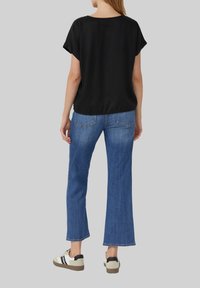 Zwarte top met korte mouwen gecombineerd met lichtblauwe wijde jeans. Schoenen zijn beige en zwart met een gestructureerde zool. Over het algemeen een minimalistisch design.
