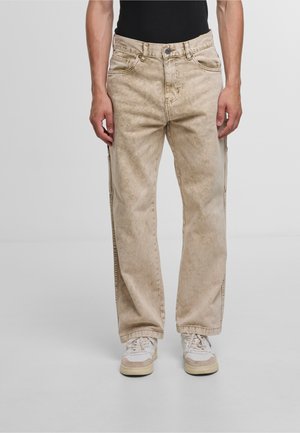 Beige denim jeans with a faded texture, straight-leg design, and five pockets, paired with white and beige sneakers.