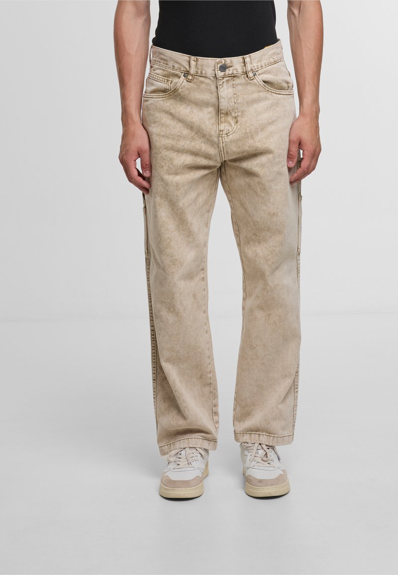 Jeans in denim beige con una texture sbiadita, design a gamba dritta e cinque tasche, abbinati a sneaker bianche e beige.