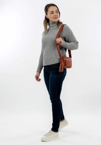 Maglione grigio a collo alto, jeans skinny blu scuro, sneaker bianche e una piccola borsa a tracolla marrone con dettagli a frangia.