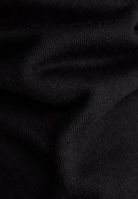 Detailní záběr na černou pletenou látku s viditelnou texturou a záhyby pod jemným osvětlením.