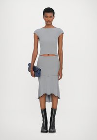 Conjunto de dos piezas gris de canalé que incluye un top corto y una falda hasta la rodilla con dobladillo acampanado. Acompañado de un bolso de mano azul y botas negras hasta la rodilla.